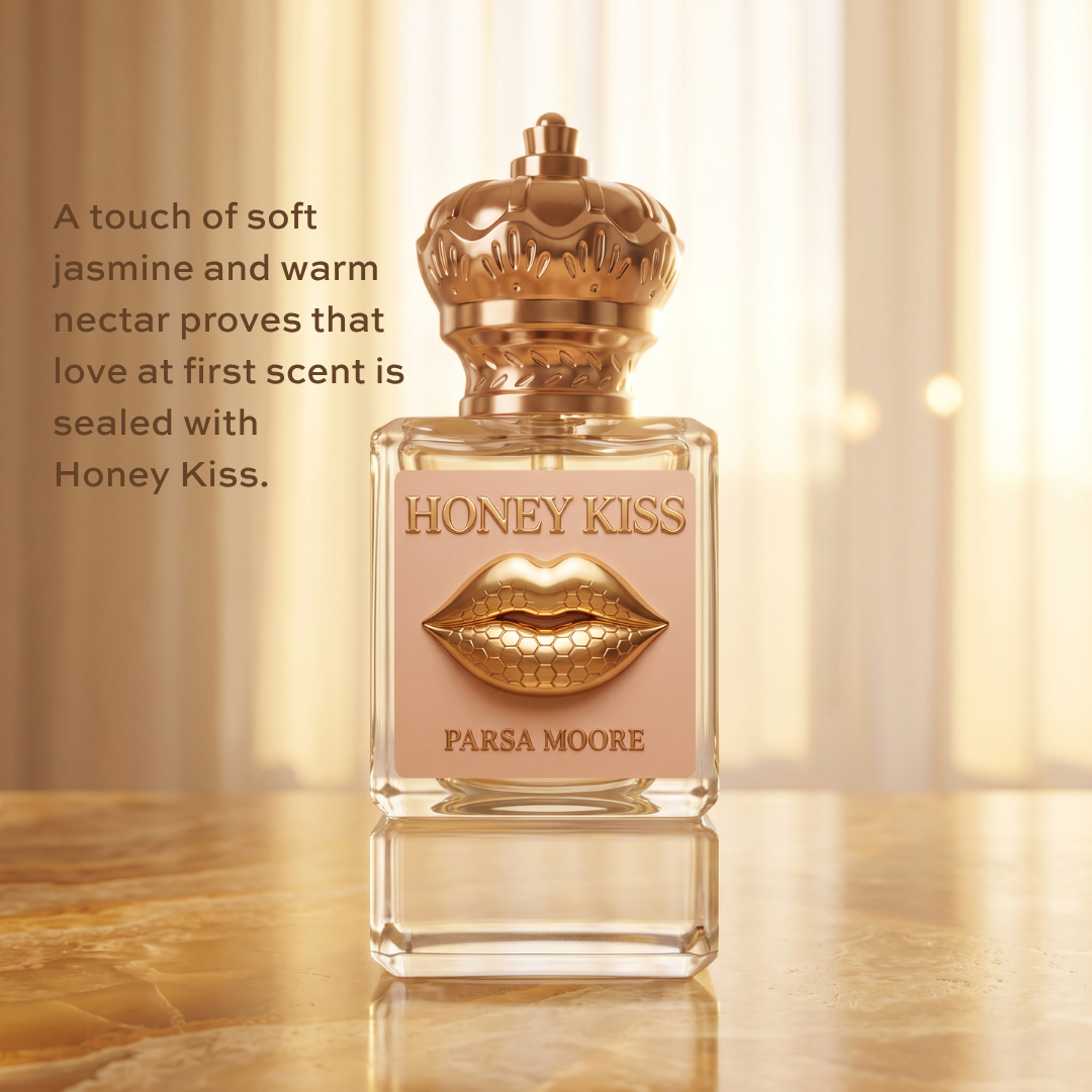 A bottle of Parsa Moore Honey Kiss perfume stands on a reflective surface against a warm, softly lit background. The bottle is clear glass with a pale pink label, a metallic gold lips emblem, and a decorative gold cap.