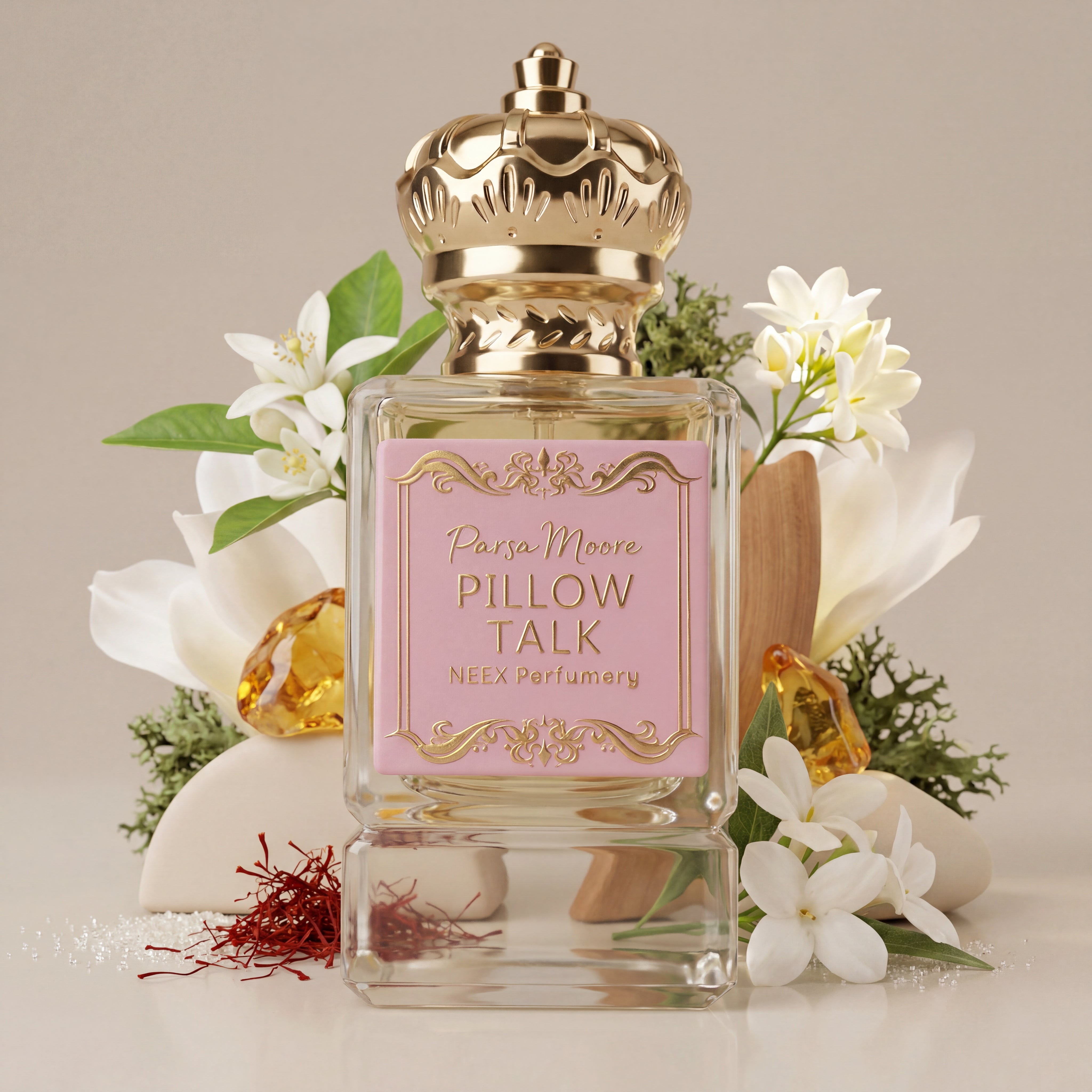 A clear glass perfume bottle with a pink label reading 'Parsa Moore Pillow Talk' and 'NEEX Perfumery,' topped with a metallic gold crown-shaped cap. The bottle is styled with white flowers, green leaves, small amber stones, and red saffron threads on a light beige background.